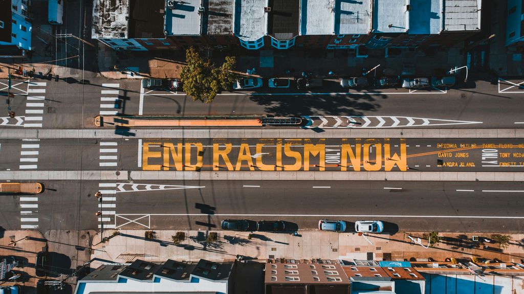 Figure 3: A birds-eye view of a mural that reads “End Racism now” painted yellow onto street pavement. Figure 3